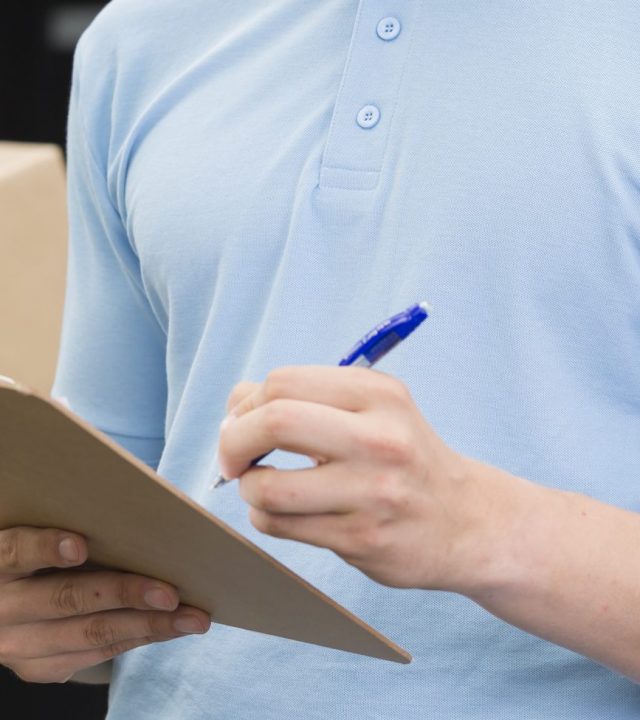 Courier filling up form Cropped shot of a courier filling up form, his colleague holding a package in the background